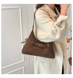 Detail of dark brown suede shoulder bag featuring a gold buckle and slim strap