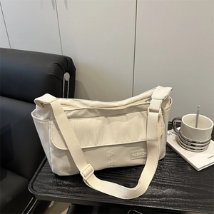 Sac bandoulière minimaliste en nylon beige sur table noire au design décontracté urbain