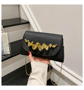 Close-up of black cross-grain leather crossbody bag with artistic wavy gold metal trim
