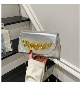 Detail van zilveren crossbodytas met goudkleurige gesp en slanke kettingriem
