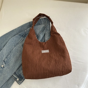 Detail der dunkelbraunen Plissee-Hobotasche mit Fashion-Patch auf Denim-Hintergrund