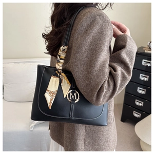 Detail van zwarte lederen tote met witte stiksels, gouden M-gesp en zijden sjaal accessoire