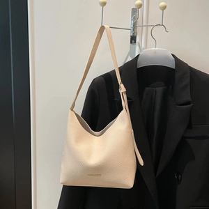 Chic cream white hobo bag with lychee texture and gold logo hanging by a suit