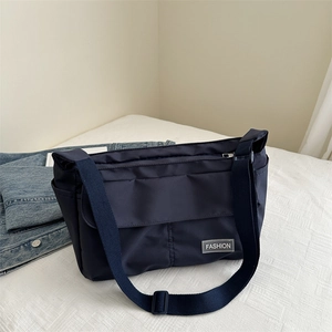 Minimalist navy blue messenger bag with adjustable strap on white bedding backdrop