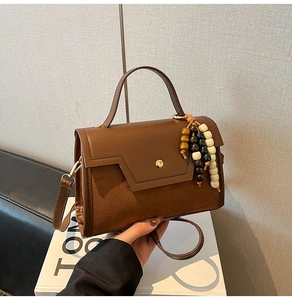 Detail of brown leather and suede baguette bag with vintage bead charm and gold buckle