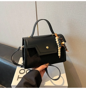 Close-up of black leather baguette bag with gold buckle and tricolor beaded tassel charm