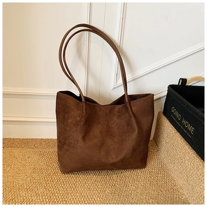 Detail view of large dark brown suede tote bag on a woven rug in a minimalist room