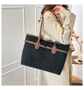 Detail of a large black suede tote bag with brown straps worn on a model's shoulder