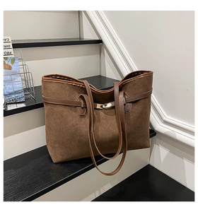 Close-up of brown suede tote bag featuring refined leather trim and gold metal buckle detail