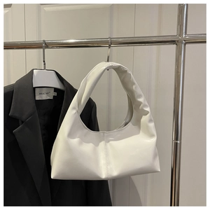 Close-up of a white patent leather hobo bag hanging on a minimalist metal stand