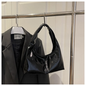 Detail of glossy black faux leather hobo bag hanging with a minimalist suit jacket
