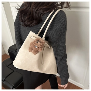 Model wearing a large beige tote bag with brown plush puppy charm on a grey sweater