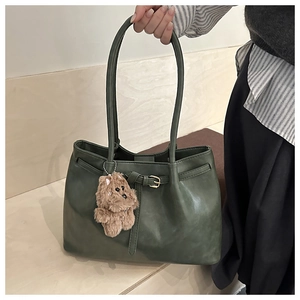 Detail of dark green tote bag with matte texture and decorative brown bear charm