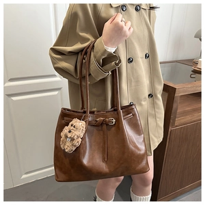Close-up of brown faux leather tote bag with stylish belt buckle and plush bear charm