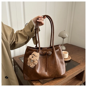 Detail of dark brown leather tote bag with belt buckle decoration and plush charm
