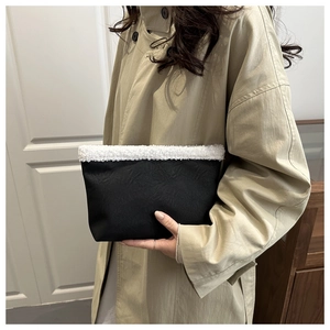 Close-up of black textured leather handbag featuring plush white faux fur trim on top