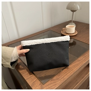 Detail of elegant black pleated faux leather clutch with white faux shearling trim
