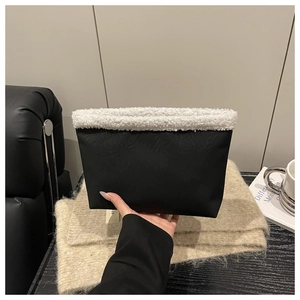 Detail of black matte plush underarm bag with white sherpa fleece trim on soft knit background