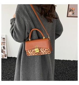 Detail of a brown leather crossbody bag with leopard print and a gold metal buckle