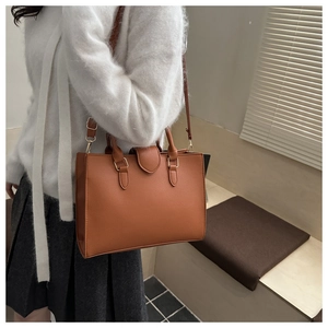 Close-up of caramel lychee grain leather texture and golden buckle on minimalist tote bag