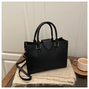 Close-up of black textured leather tote bag on beige scarf with light gold hardware