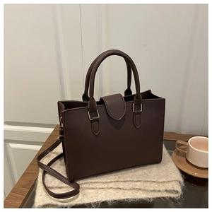 Detail of dark brown lychee textured handbag with gold hardware on soft fabric