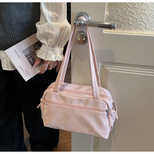 Detail of light pink nylon tote bag with multiple zipper pockets hanging on a door handle