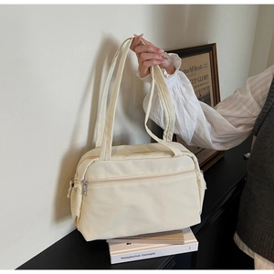 Close-up of a cream nylon tote bag with front zipper pocket held by hand in a minimalist setting