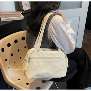 Close-up of a white canvas tote bag with zipper pocket worn by a model in a cozy setting