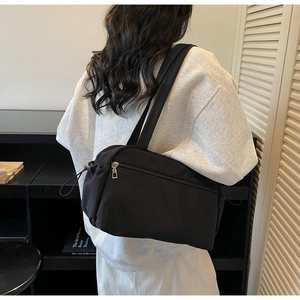 Rear view of a black canvas tote bag worn by a model, showing urban commuting style
