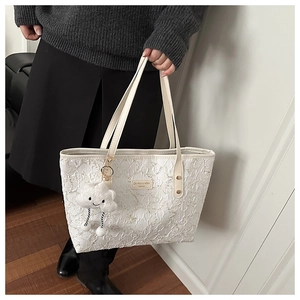 Close-up of white embossed tote bag with plush cloud charm and leather handle