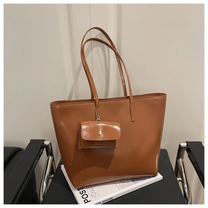 Detail of glossy brown tote bag with mini charm pouch on a black chair with magazine