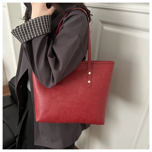 Detail of red tote bag with lychee texture and gold rivet hardware on shoulder strap