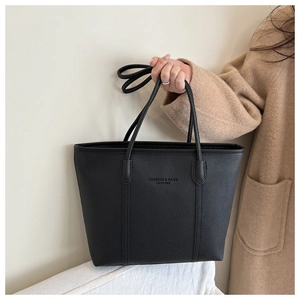 Detail of minimalist black leather tote bag with embossed text and pebble texture