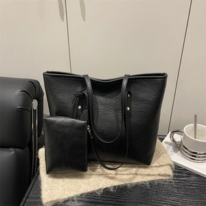 Minimalist black faux leather tote bag set with matching pouch on cozy beige knit blanket