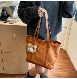Detail of brown suede tote bag with leather handles and a cute teddy bear charm