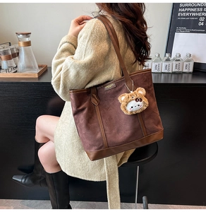 Chic brown suede tote bag with leather handles and cute plush charm on a model