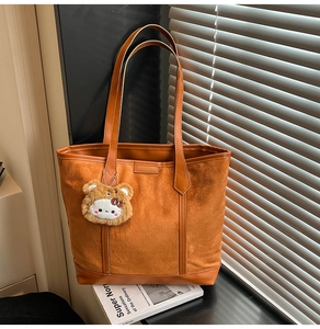 Close-up of a brown tote bag with suede texture and a cute plush kitty charm on the handle