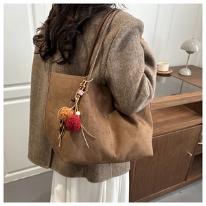 Brown suede tote bag detail with decorative tassel charm and cylindrical shoulder strap
