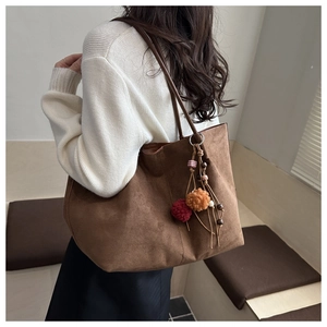 Close-up of brown suede tote bag with colorful pompom charms and wooden beads