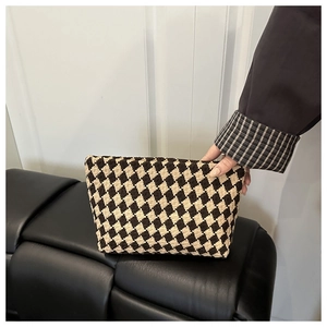 Close-up of retro brown plaid woven makeup bag held by hand in a minimalist interior