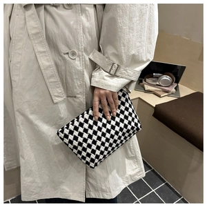 Detail of checkered woven pouch with textured pattern held against a beige trench coat