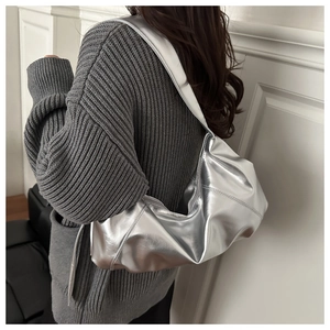 Close-up of metallic silver underarm bag with glossy finish on grey knitted sweater