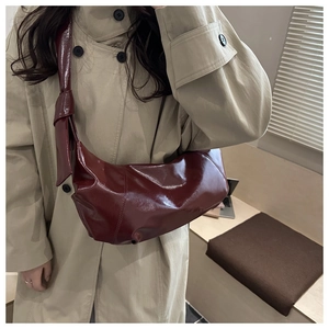 Close-up of a burgundy patent leather crescent bag with unique knotted strap detail