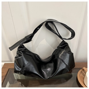 Detail of black glossy faux leather shoulder bag with decorative strap knot on a table