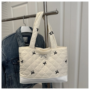 Detail van crème gewatteerde tote bag met zwarte strikborduursels en zilveren hanger