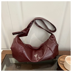 Close-up of a burgundy glossy leather handbag featuring a stylish side knot detail design