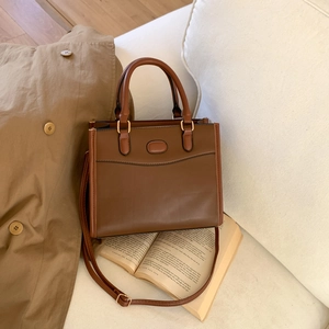 Retro brown contrast stitch handbag with gold hardware and adjustable strap on beige coat