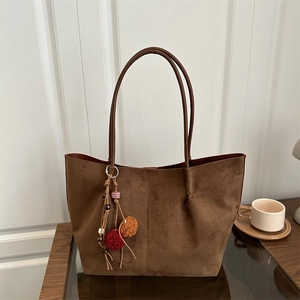 Large vintage dark brown suede tote bag with ethnic tassels on a wooden table