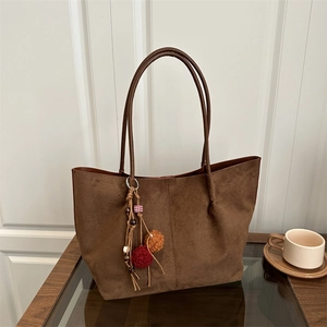 Brown faux suede tote bag with ethnic pom-pom charm and large capacity on white background